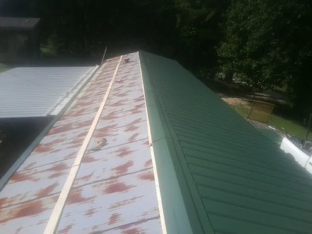 Old rusted panels beside newly installed green metal roofing — Wind Damage Roof Repair by Roofing Brothers in Osceola