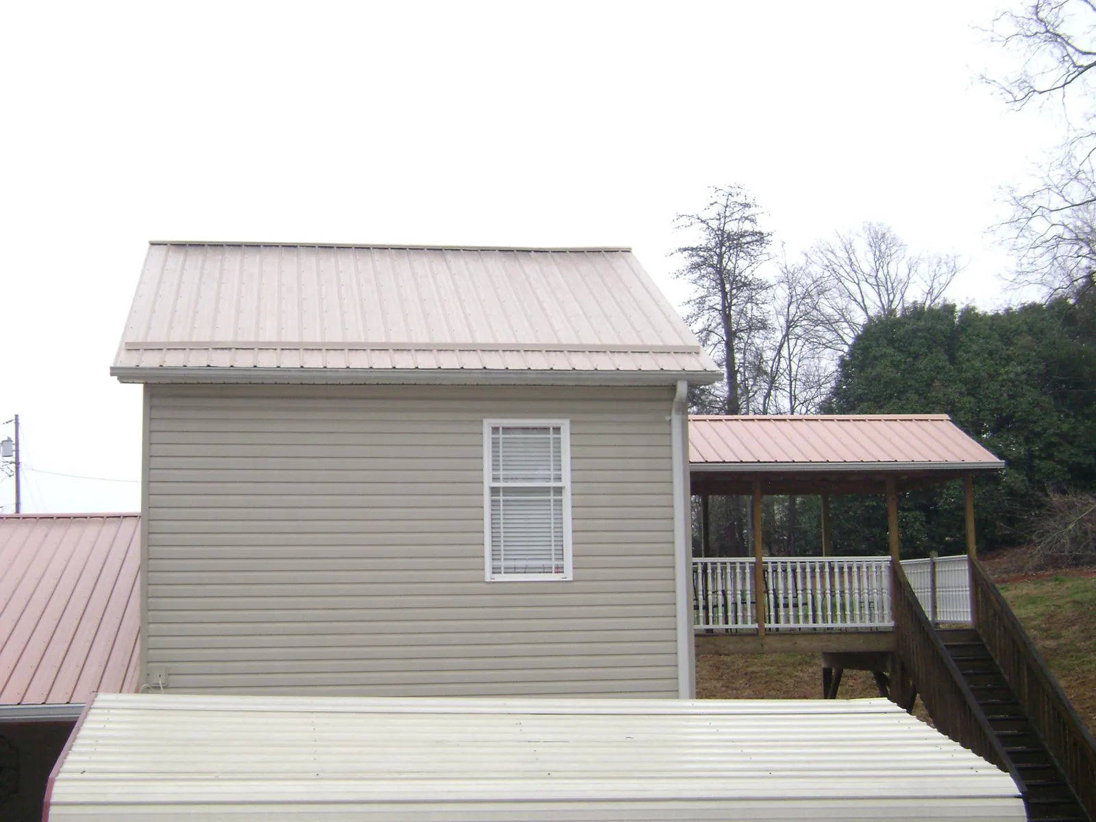 Tan metal roofs on a two story addition and attached porch, from a Roof Replacement job in Osceola